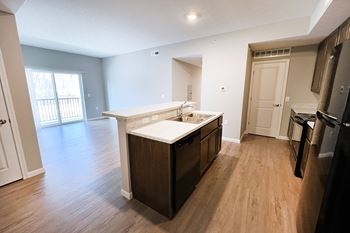 An empty kitchen and living room with wood flooring and a large window